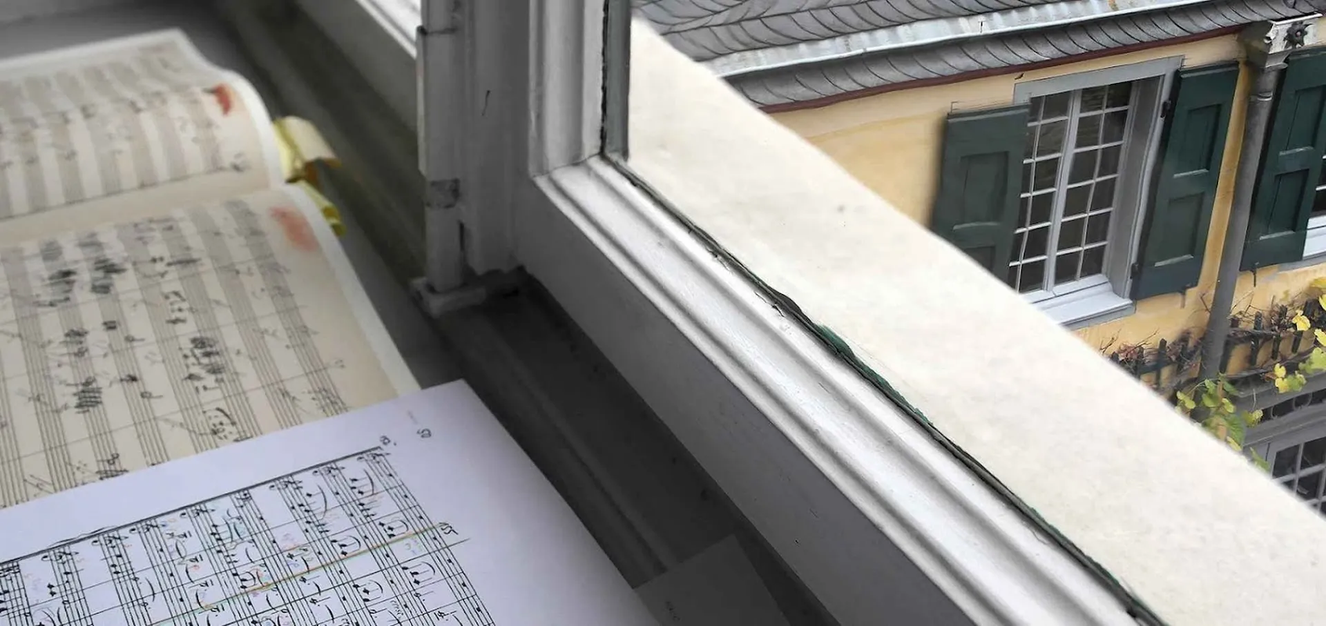 Auf der Fensterbank eines Büros liegen Noten. Durch das Fenster sieht man auf Beethovens Geburts- und Wohnhaus.