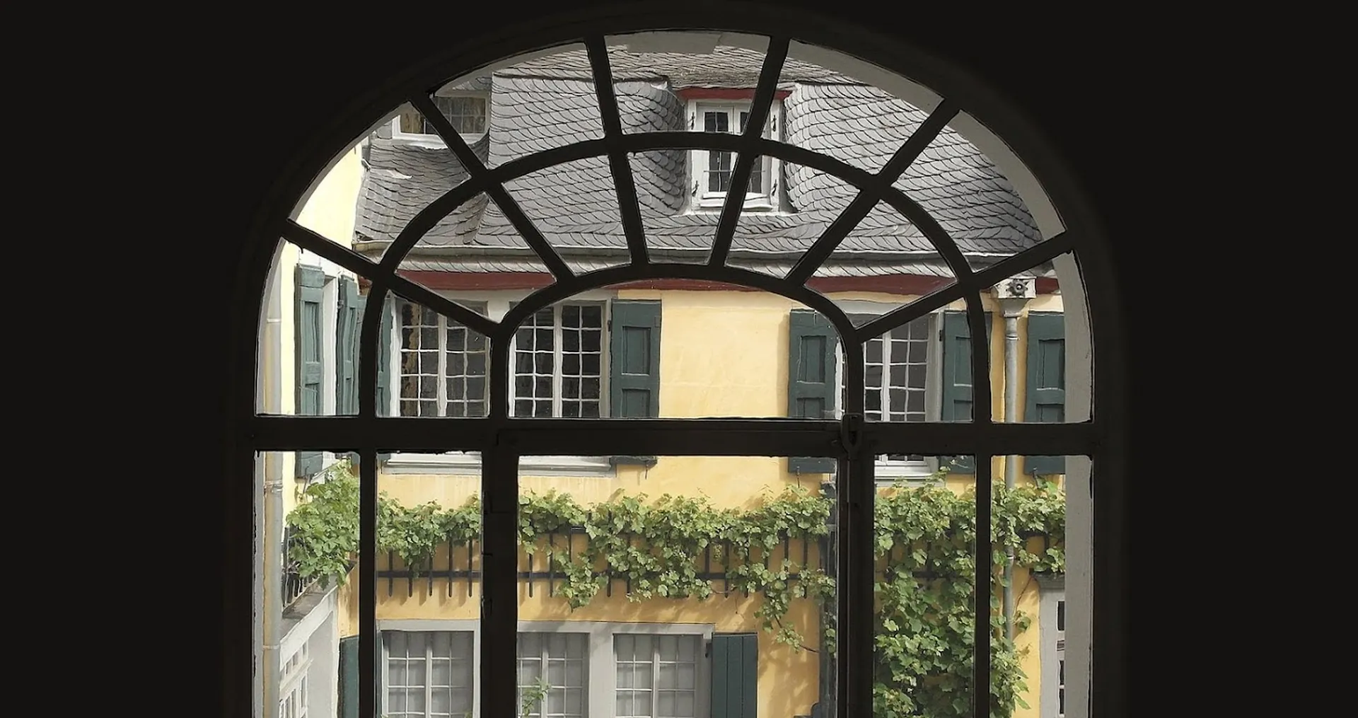 Through the arched struts of a window you can see the yellow façade of Beethoven's birthplace and home, the rear building at Bonngasse 20.