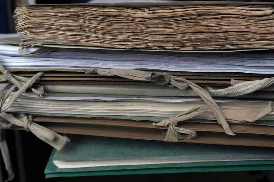 Seitenansicht auf einen Stapel mit Arbeitsmaterialien: Notenbände und graue, mit Schleifen zusammengebundene Mappen.