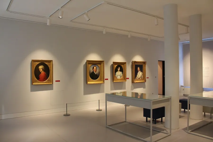 Museum room with table showcases, on the wall four illuminated portrait paintings of Beethoven's friends in gold coloured frames.